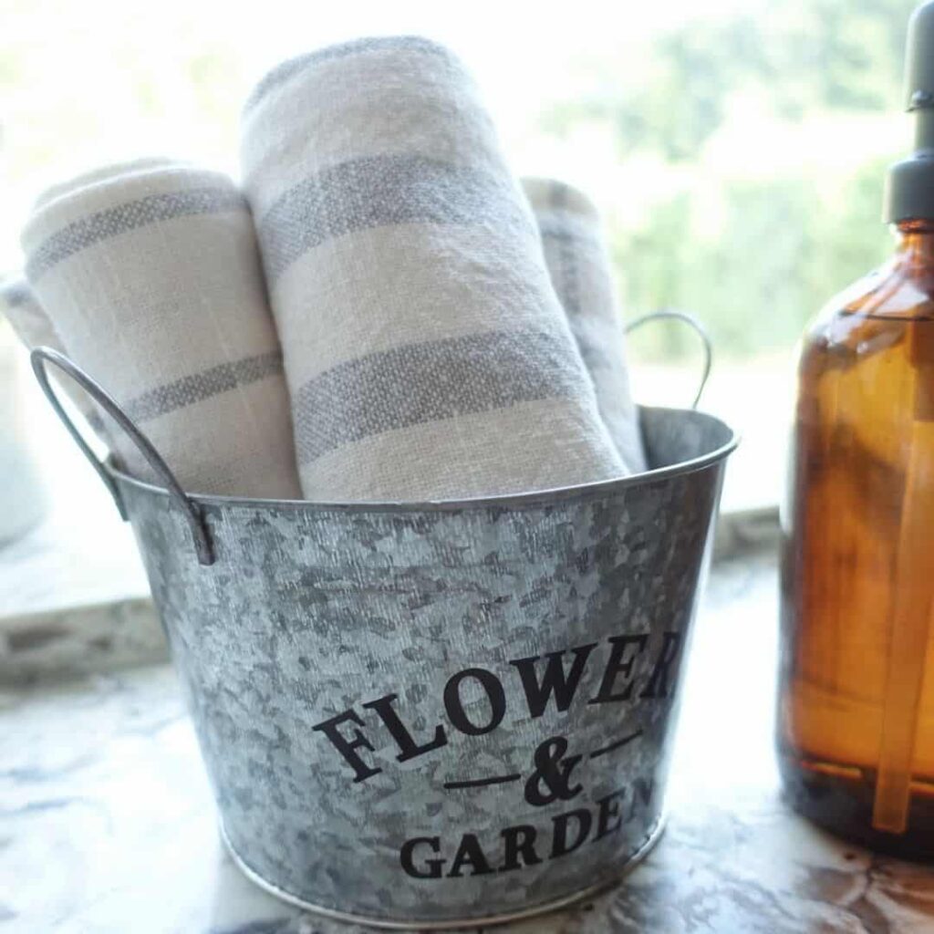 galvanized bucket from the dollar store storing striped tea towels sitting next to amber soap jars