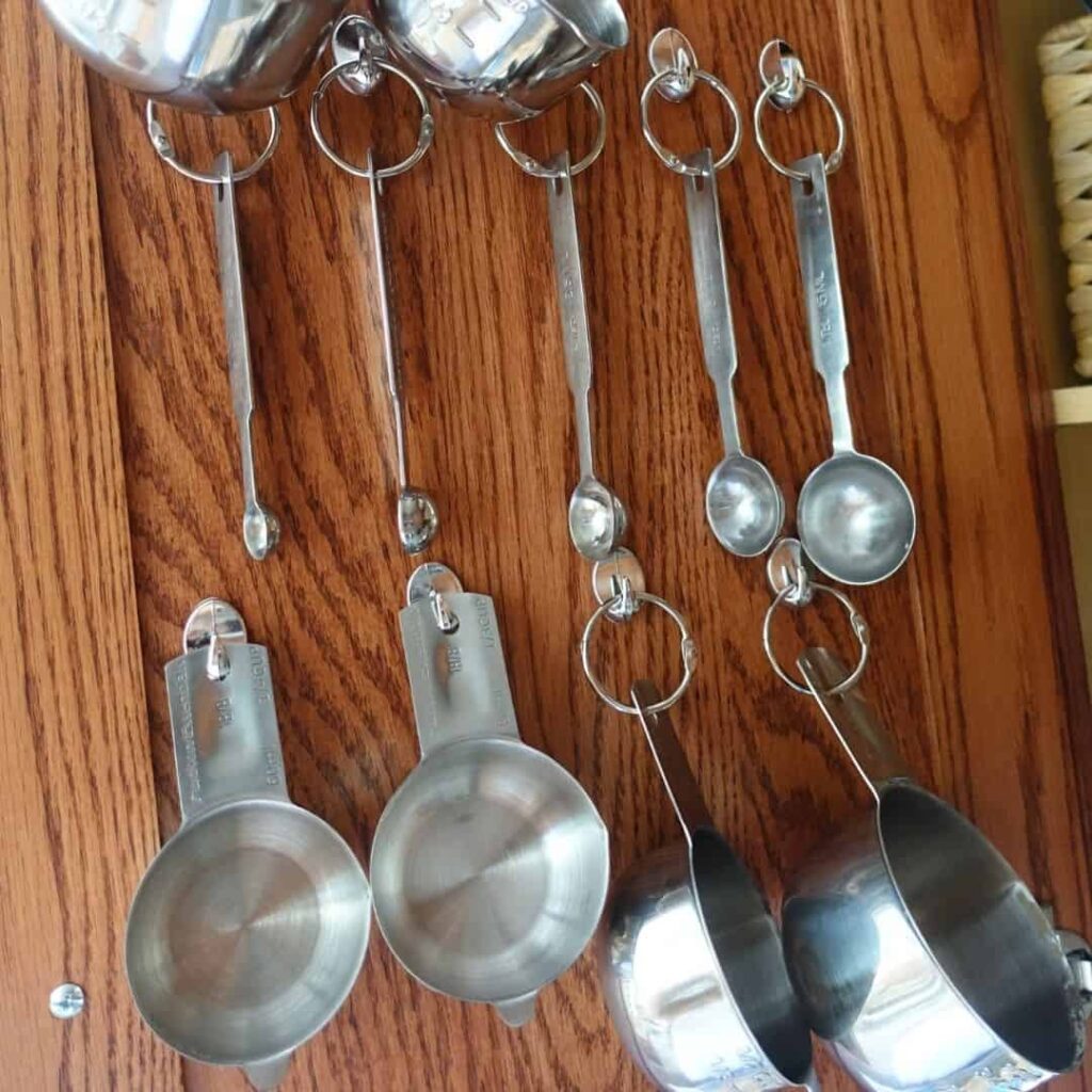 hanging measuring spoons from a cabinet on dollar store hooks and book rings