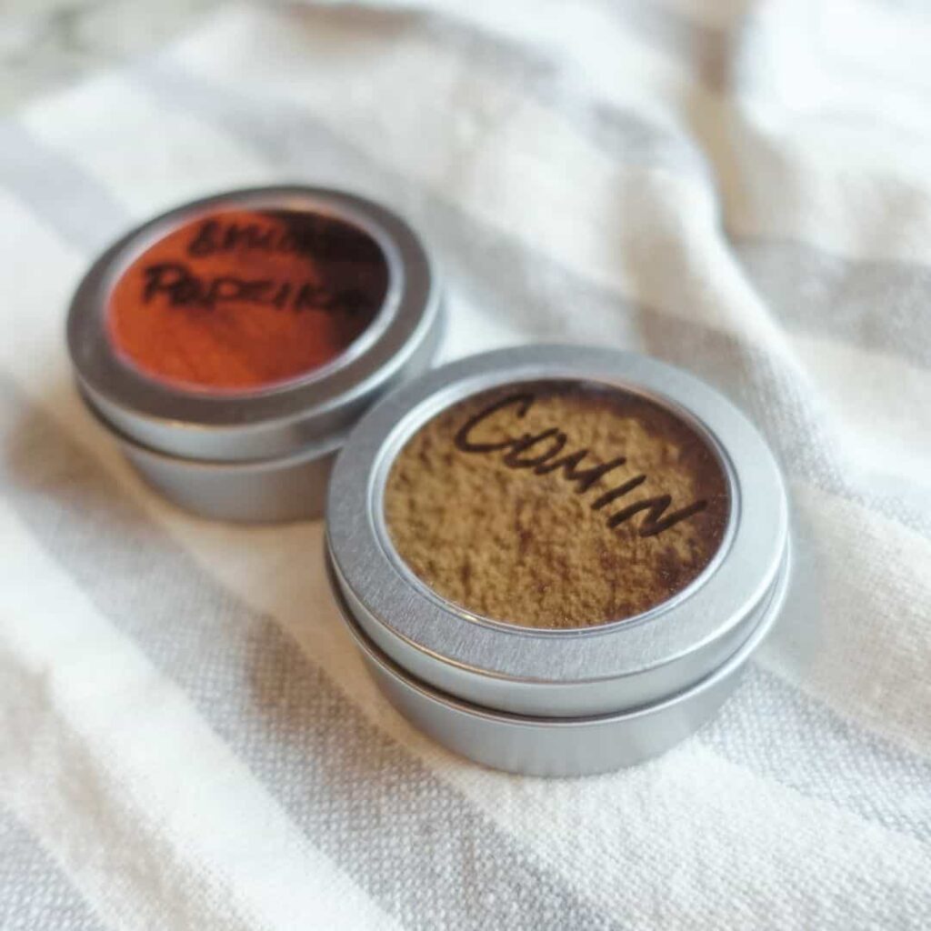 cumin and smoked paprika inside dollar store containers on top of a striped tea towel