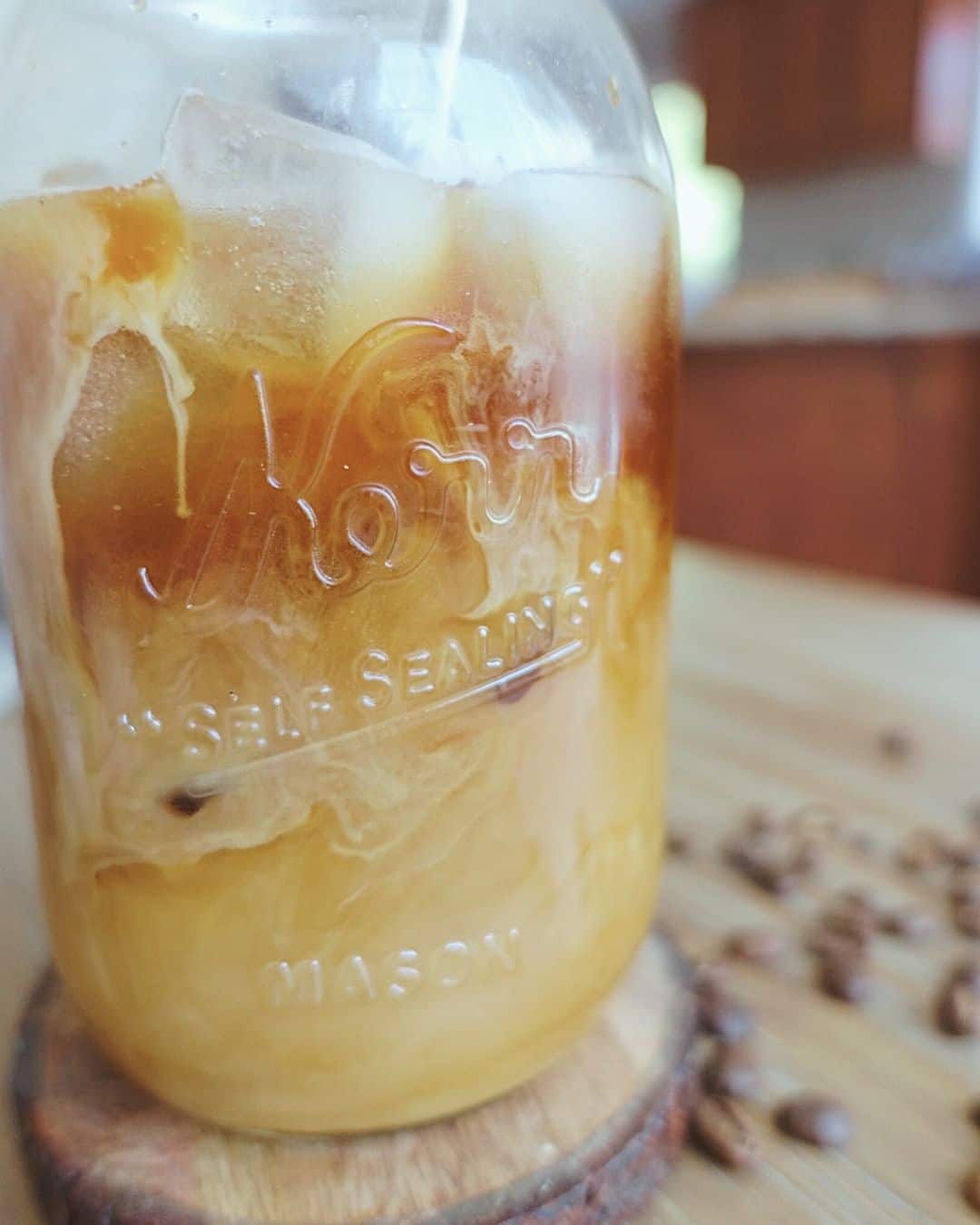 iced coffee with cream in mason jar with coffee beans surrounding it
