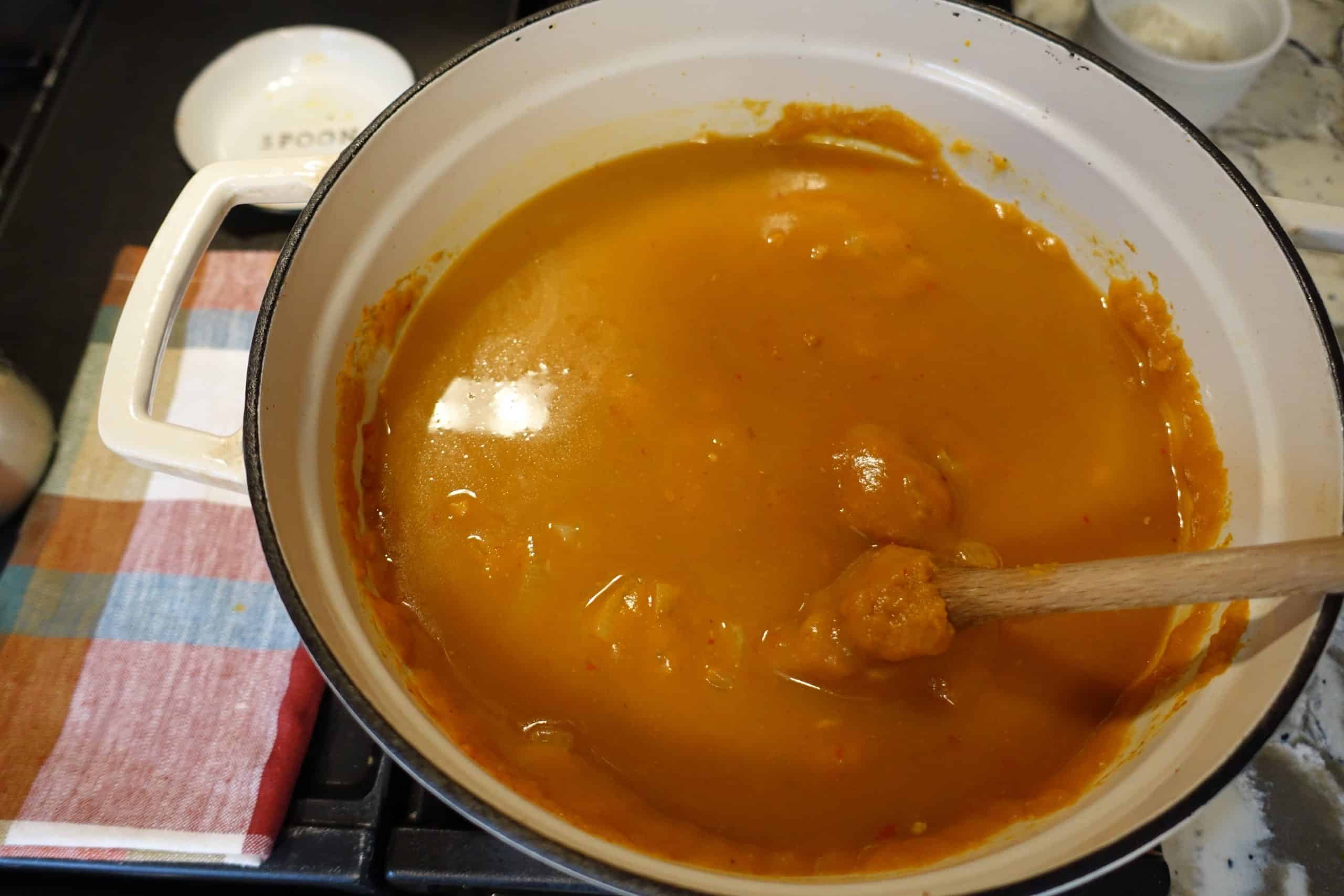 heart healthy spiced pumpkin and chorizo chili in white dutch oven with bone broth and pumpkin mixed in with wooden spoon