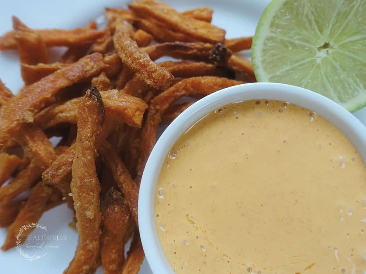 ancho aoili in a white dish with sweet potato fries and lime in the background