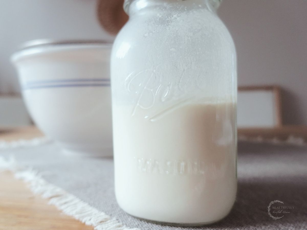 raw kefir in a mason jar on top of a grey placemat in front of a ceramic bowl with blue stripes