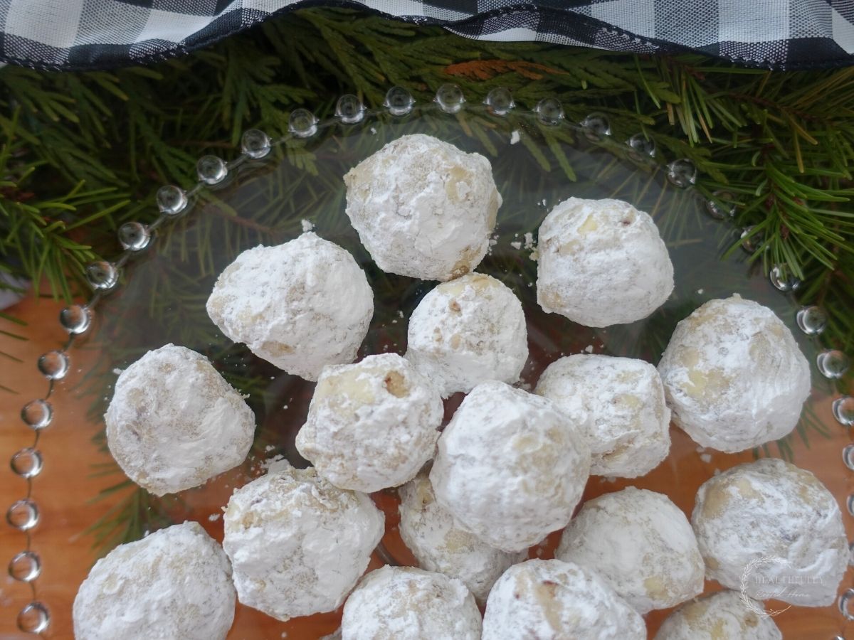 pecan meltaway cookies on a glass cake stand next to fir tree branches with a checkered white and black ribbon