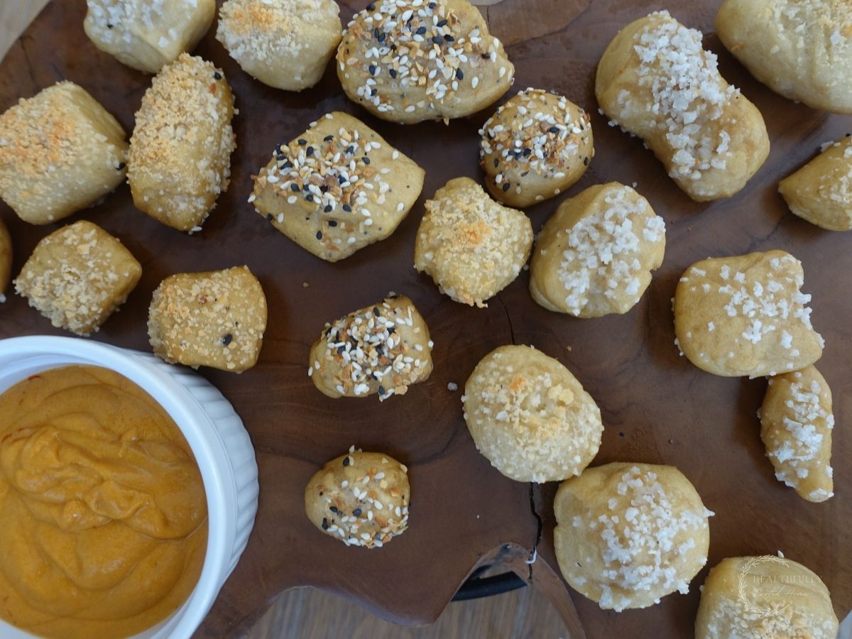 sourdough pretzel bites baked to golden brown topped with seasonings and placed on a wooden block next to cheese sauce