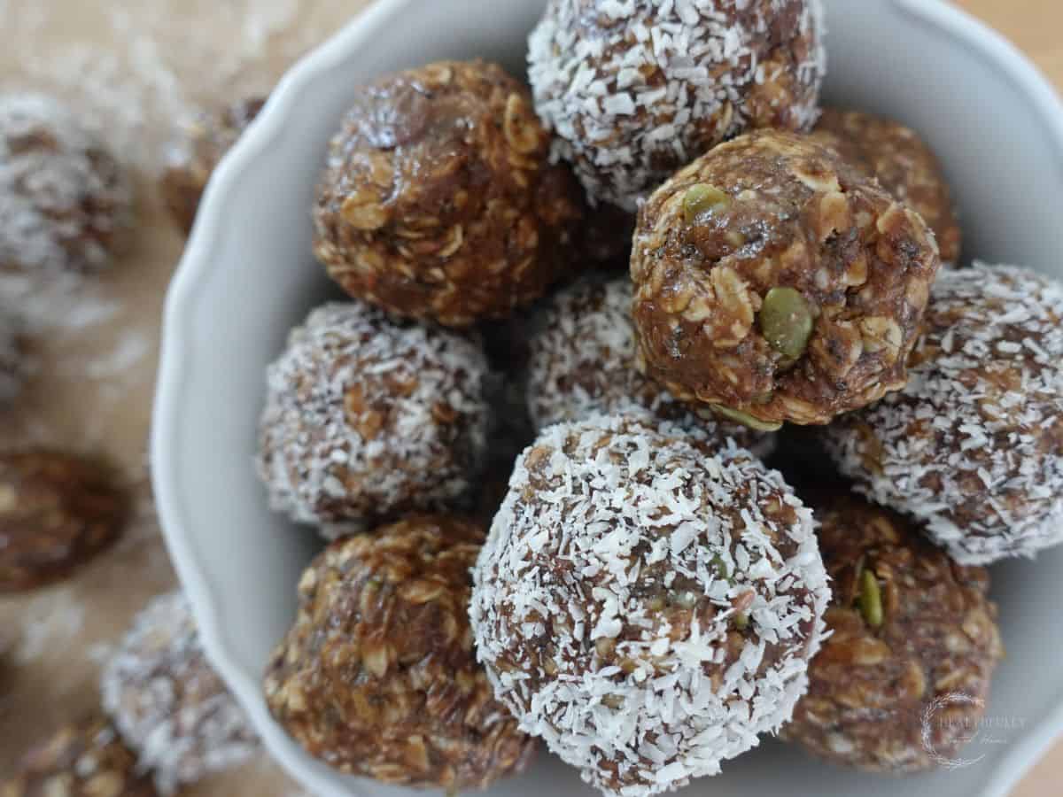 no bake boobie balls in a white bowl with half covered in coconut flakes and half not