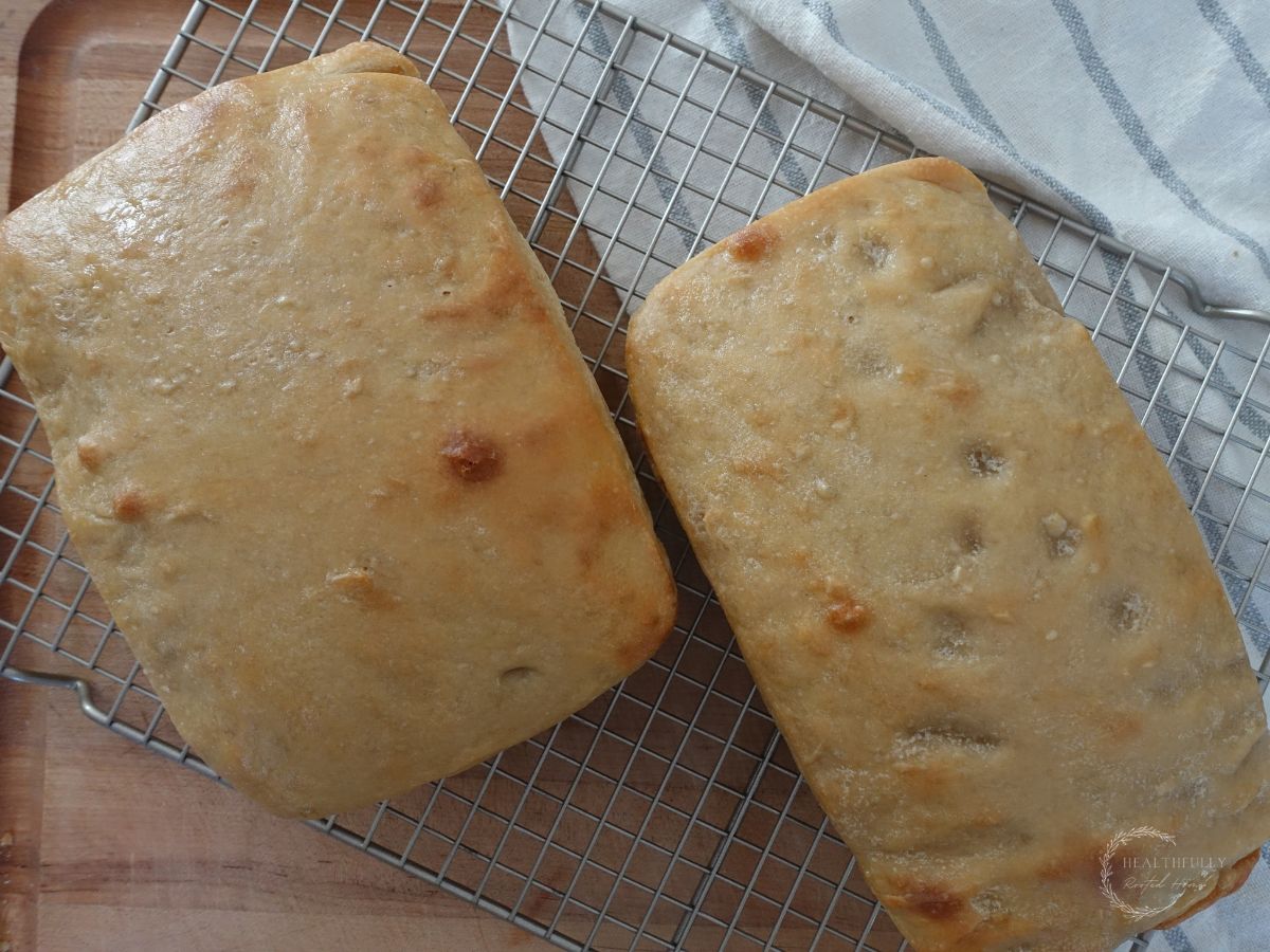 fermented bread loaves on a wire cooling rack with a striped tea towel underneath