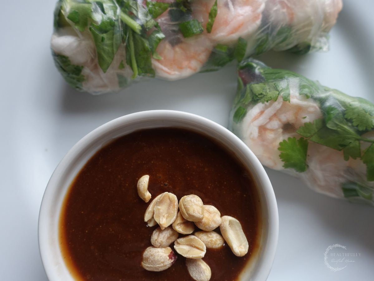 hoisin peanut sauce in a white bowl with chopped peanuts as the garnish and homemade spring rolls on the side
