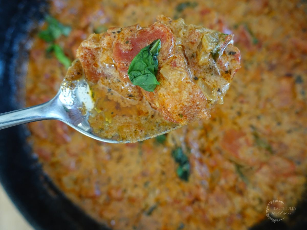 tomato mascarpone sauce in a cast iron skillet with a spoonful of sauce close up and a piece of basil on top