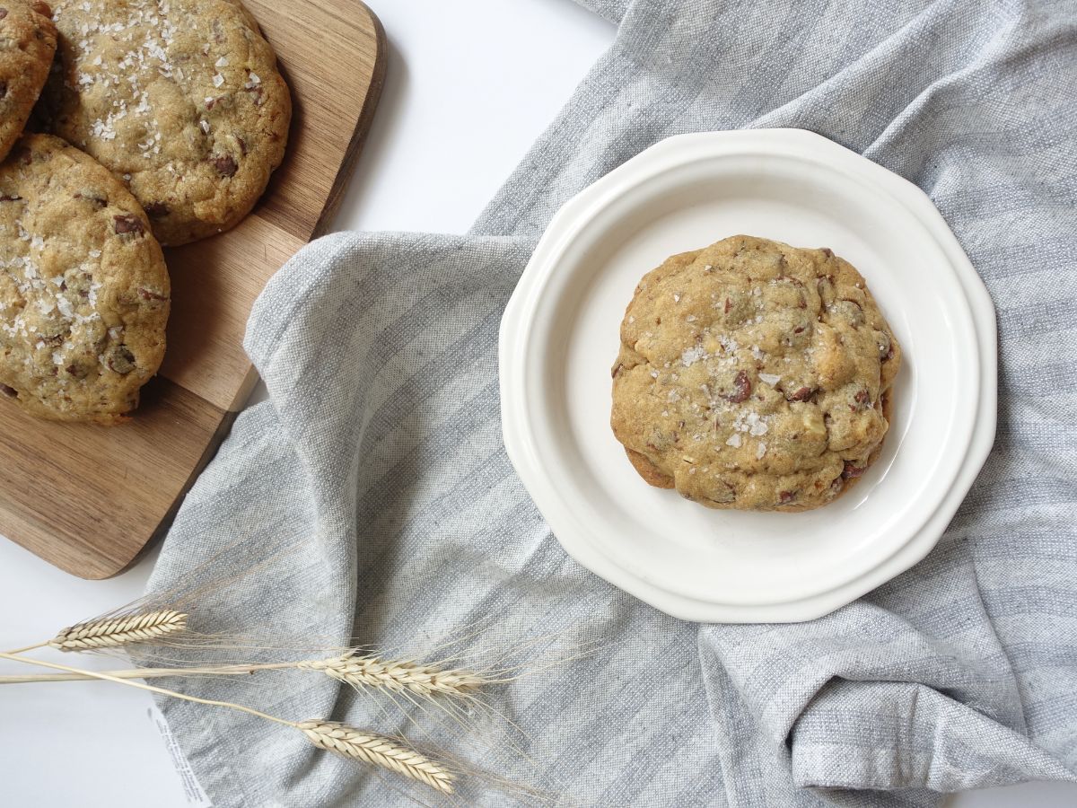 cookies without brown sugar on a white plate with a bunch stacked next to it on a wooden serving board with a tea towel underneath and wheat next to it