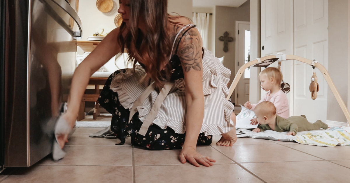 homemaker on the ground cleaning her fridge with an apron on and children playing in the background