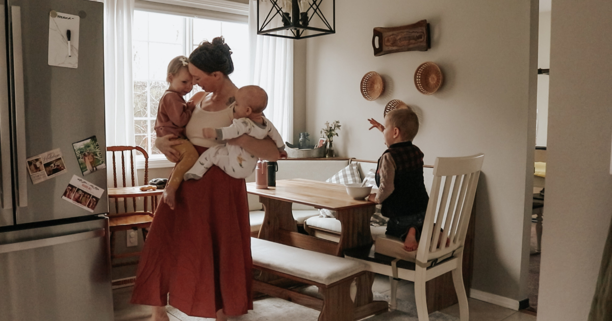 mother holding two children with one child sitting in booster seat