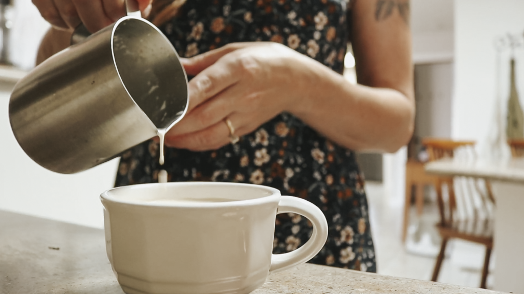 Close up of a Christian homemaker wearing a floral dress pouring frothed milk into a coffee mug.