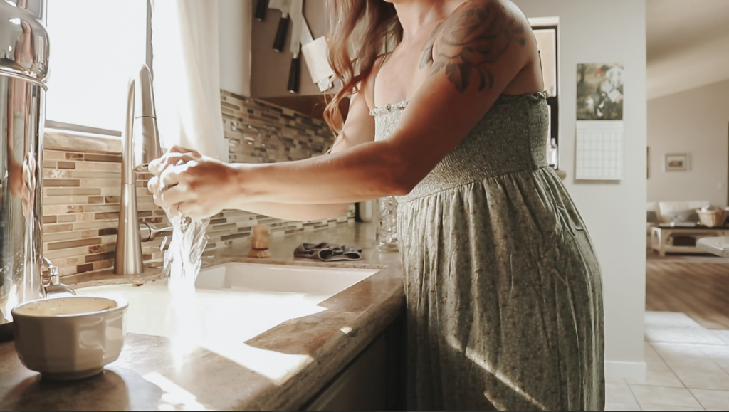 Close up of a Christian homemaker wearing a light green dress and washing her hands at the kitchen sink.