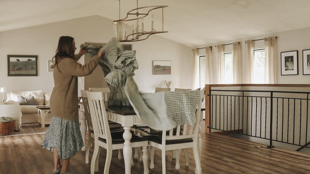 Christian homemaker is unfolding a table cloth to put on her dining room table.