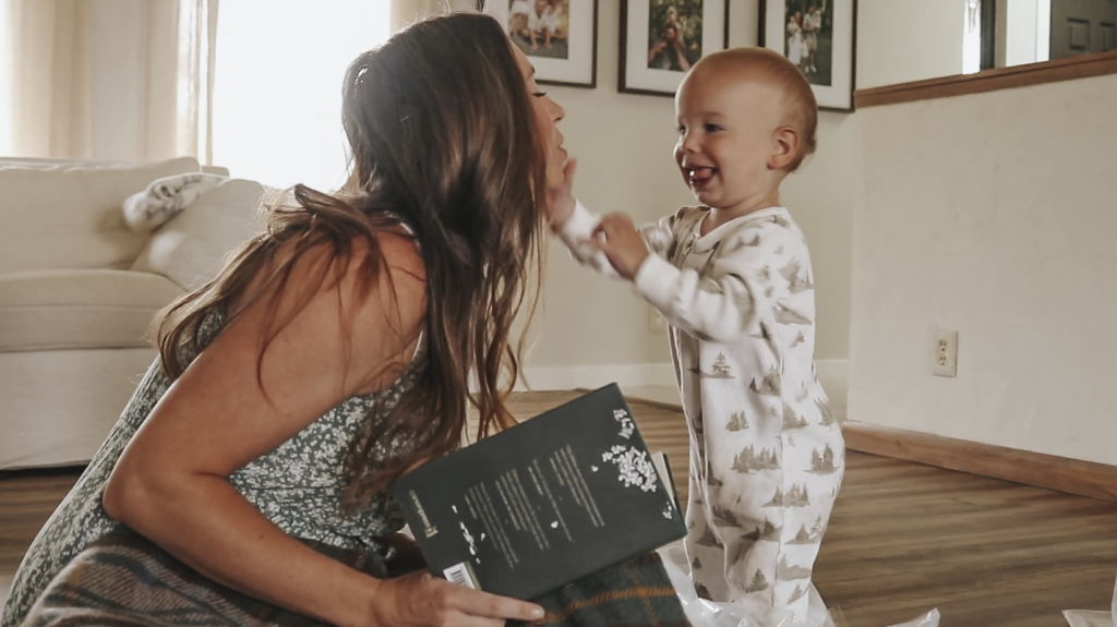 Christian homemaker wearing a floral dress is looking into her toddlers eyes and smiles as he reaches out and touches her face.