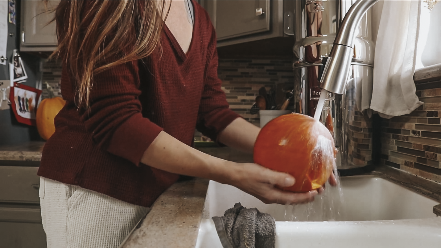 Christian homemaker stands at the kitchen sink rinsing off a pumpkin.