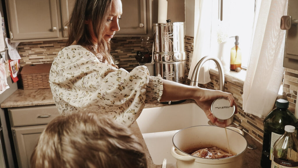 Homemaker in long, flowy dress puts ingredients into a white pot.