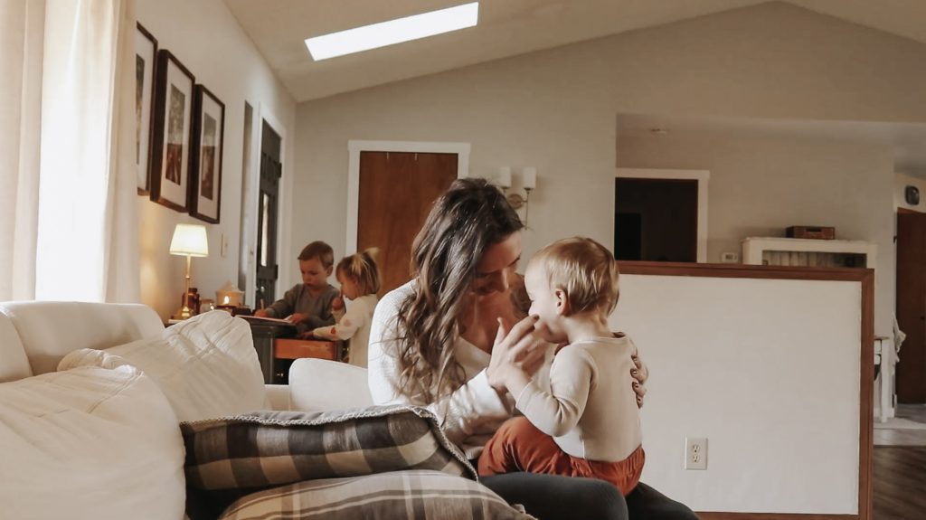 Homemaker and mother sits on a white couch with her baby.