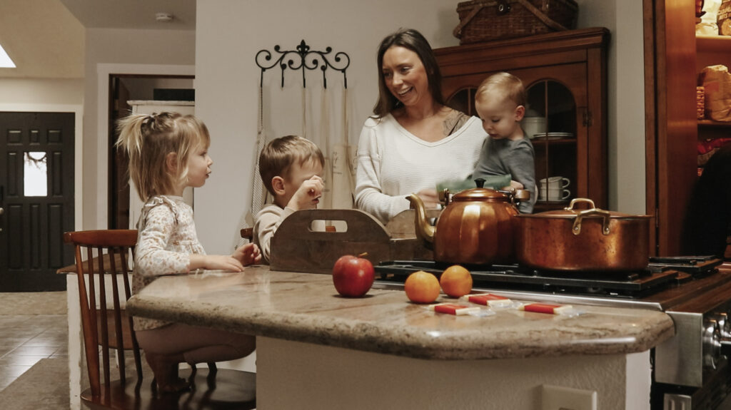 Christian homemaker and mother stands in kitchen at counter with her three children.