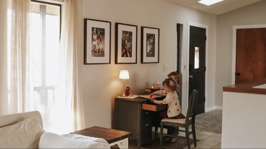 Homemaker and mother looks over her children as they sit at a desk and write.