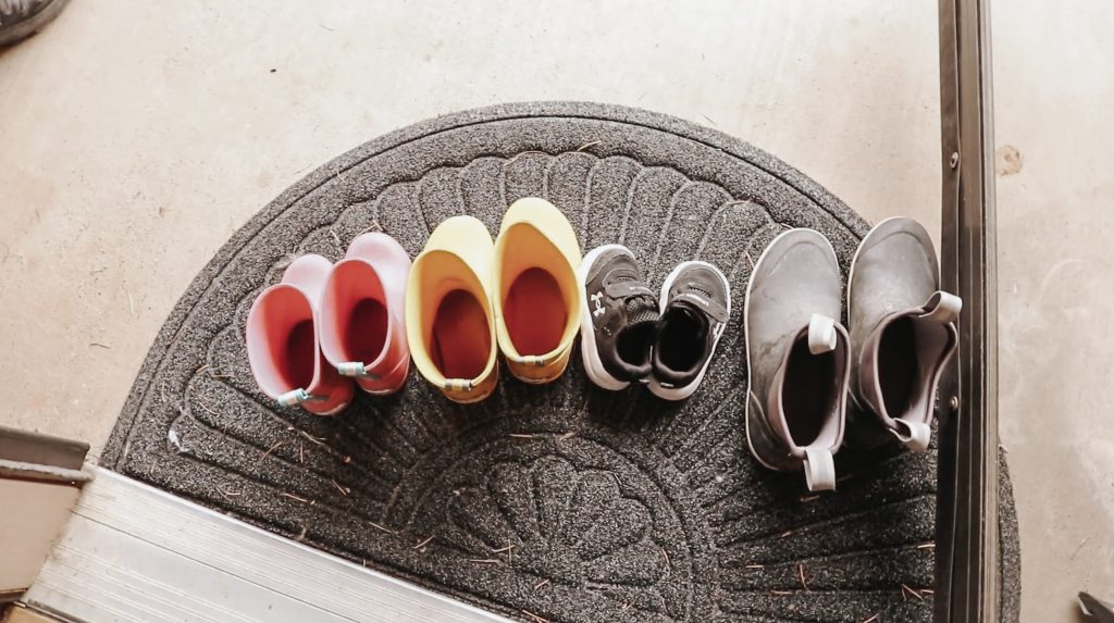 A row of outdoor shoes sits on a doormat outside.