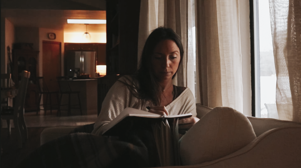 Christian mom journals in the early morning sitting in a dimly lit house with an open journal in front of her
