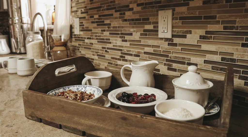 A tray of oatmeal toppings including nuts, raisins and a pitcher of cream are sitting on a tray on the kitchen counter.