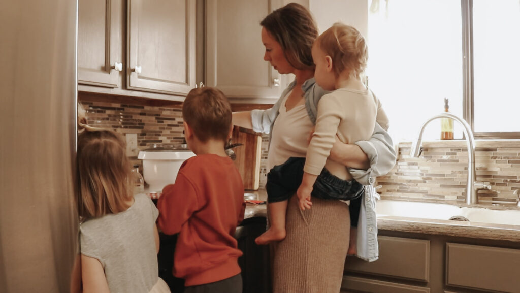 Christian homemaker and mother stands at kitchen counters with her three children.