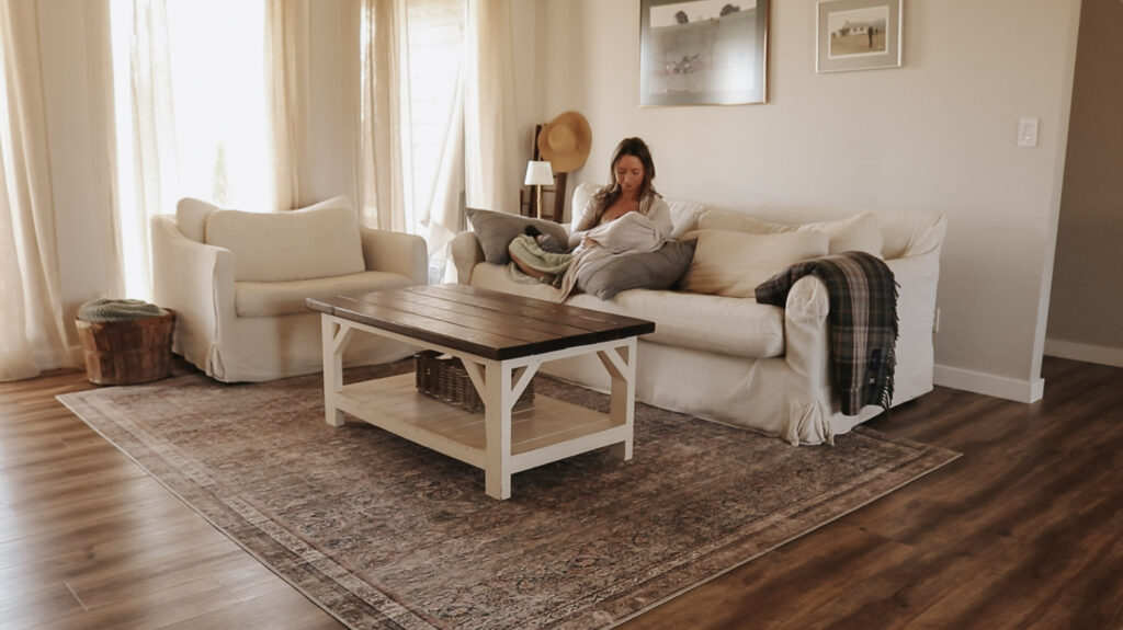 Christian homemaker sits with child on white furniture in bright, airy living room.