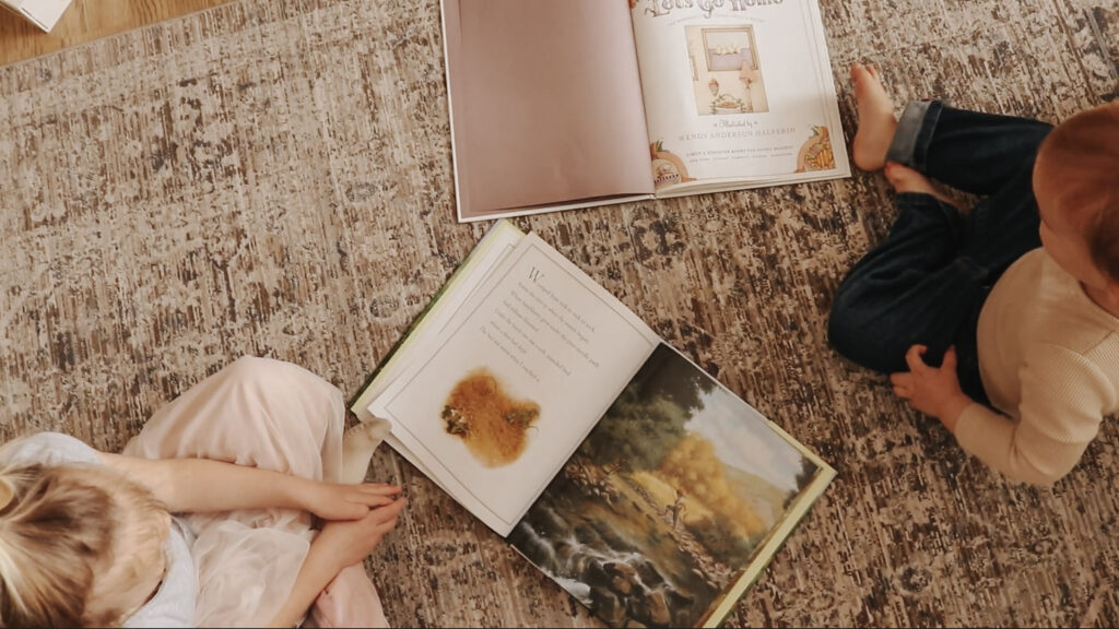 Children sit on floor surrounded by open books to read.