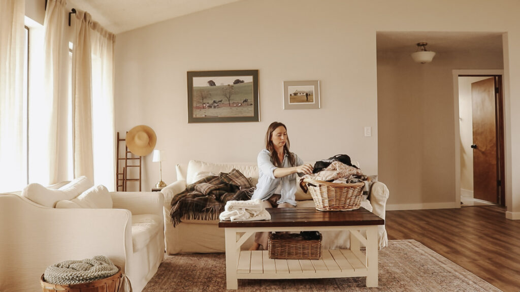 Homemaker and mother folds laundry out of a wicker basket while sitting in a bright and airy room.