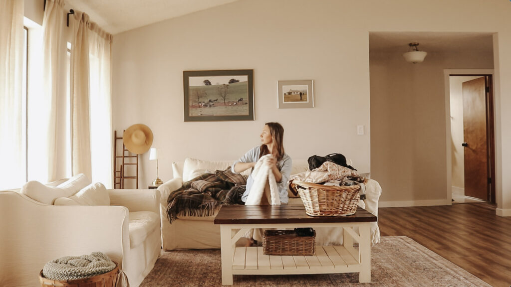 Homemaker and mother folds laundry out of a wicker basket while sitting in a bright and airy room.