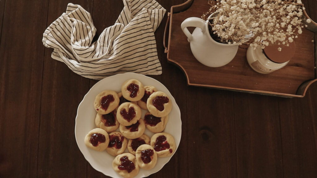 Cookies, a kitchen towel, and flowers sit on a wooden table.