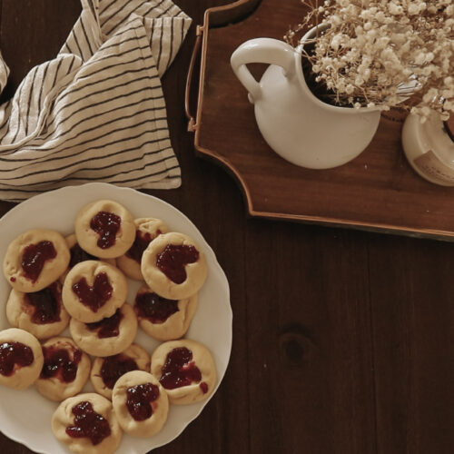Cookies, a kitchen towel, and flowers sit on a wooden table.