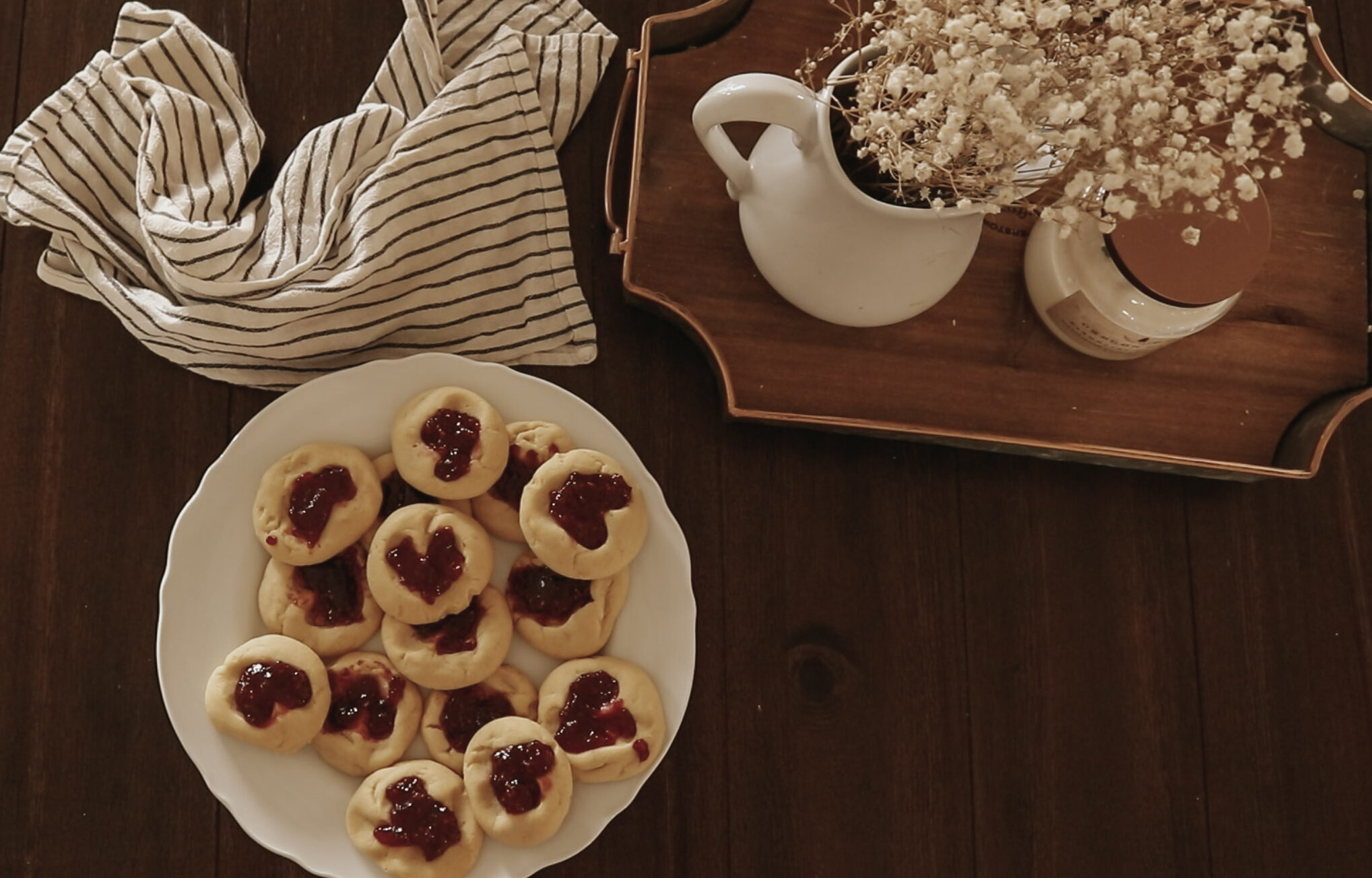 Cookies, a kitchen towel, and flowers sit on a wooden table.
