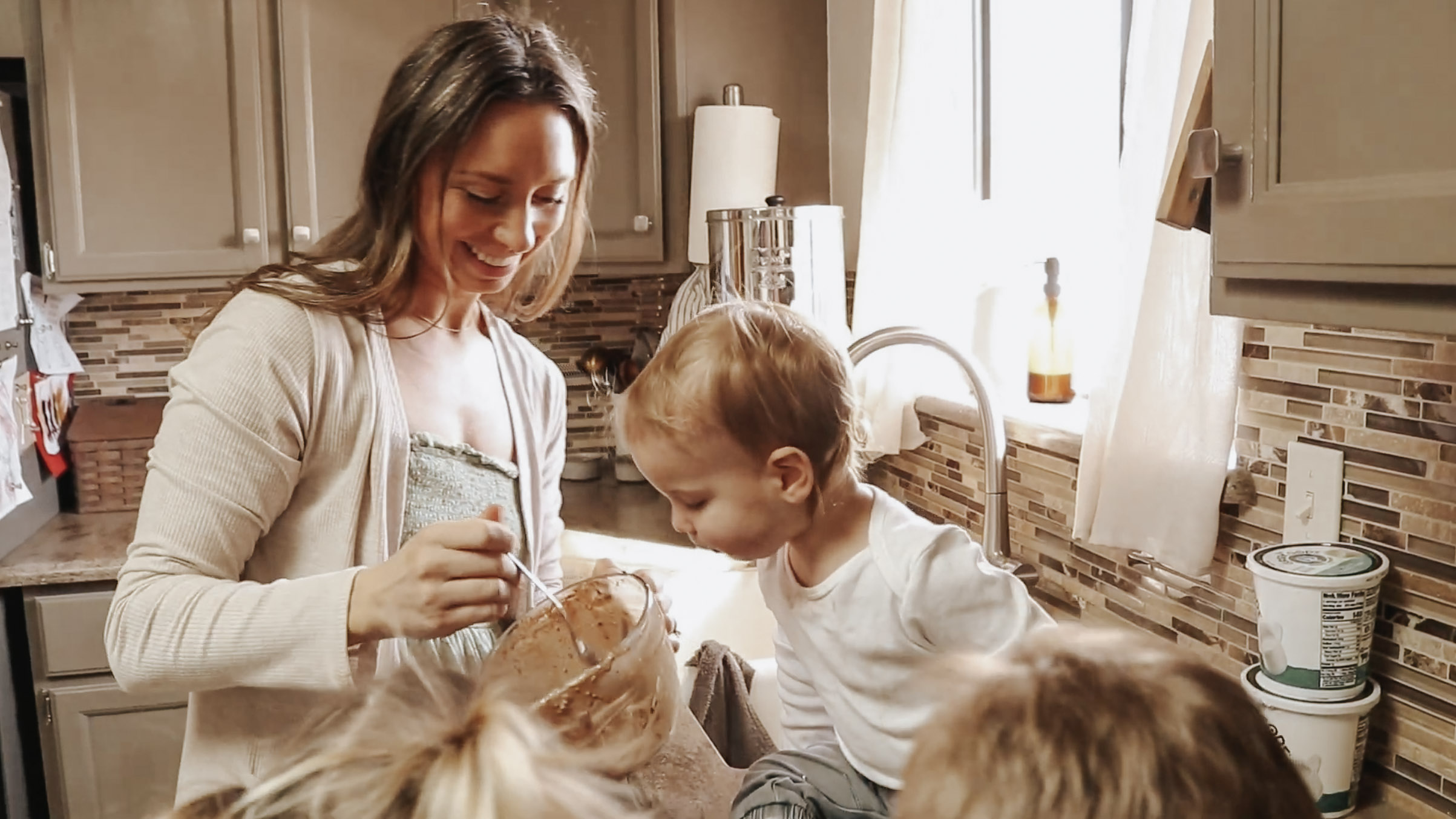 Homemaker and mother stands with children at counter with snack.