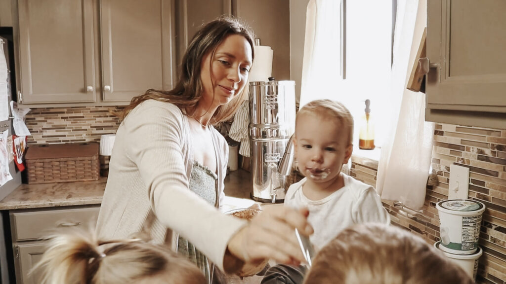 Christian homemaker and mother stands with children and gives them a bite of a snack.