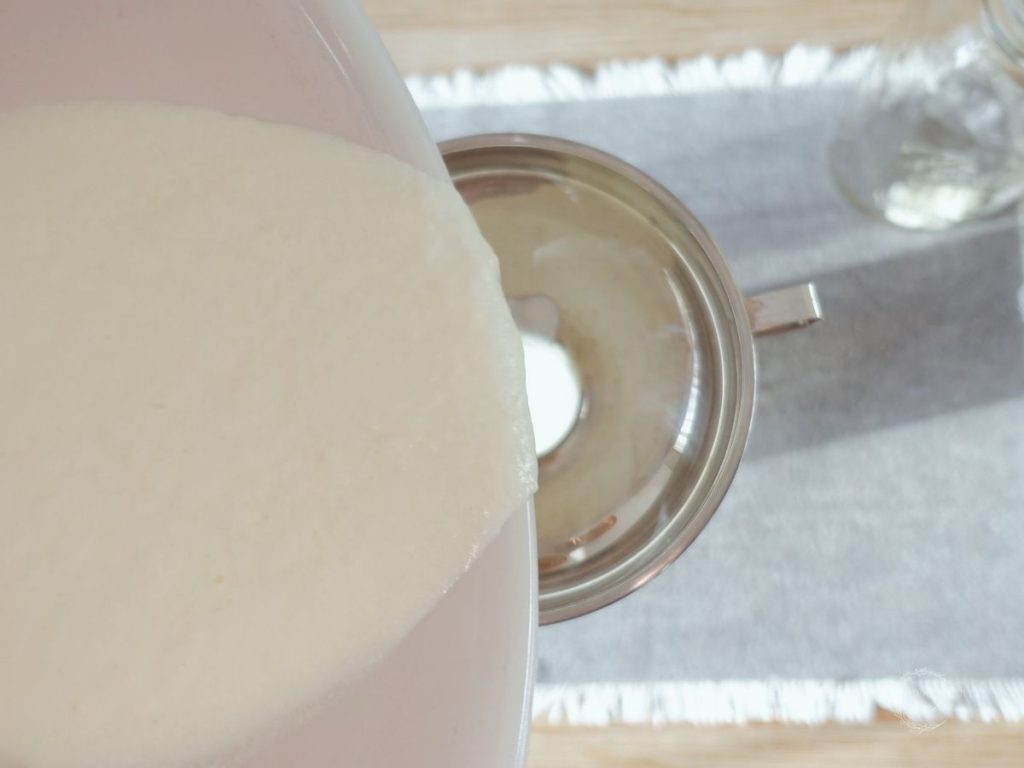 pouring raw kefir into a mason jar through a canning funnel on top of a grey placemat next to a mason jar with kefir grains inside