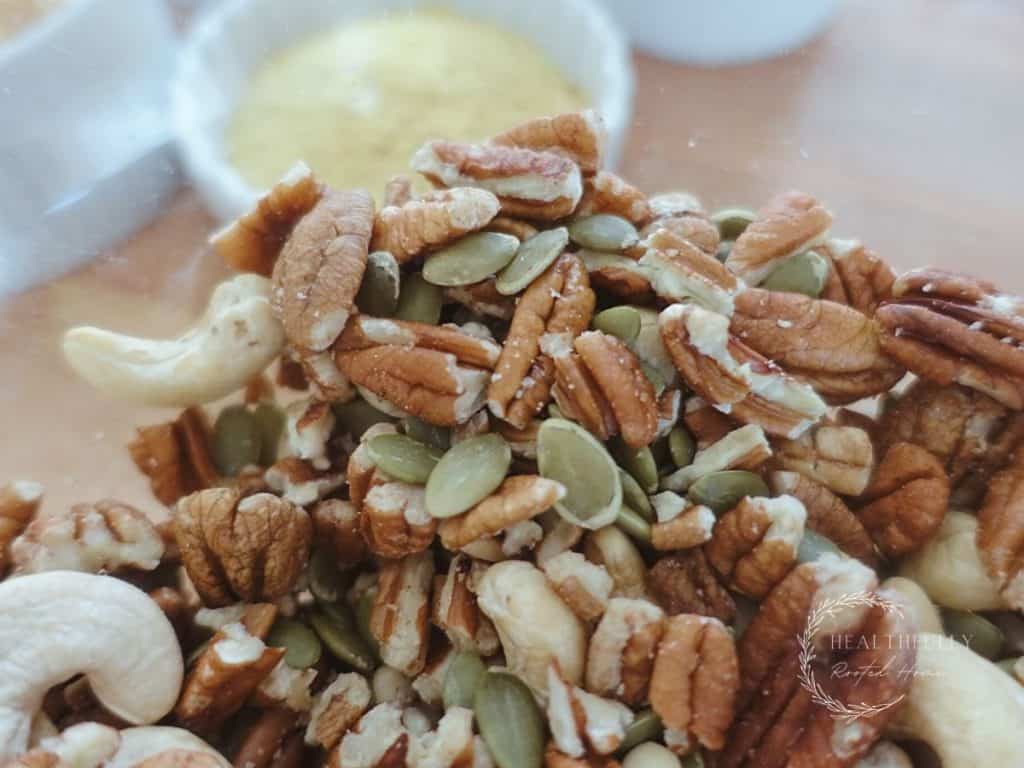 pecans cashews and pepitas in a large glass bowl with nutritional yeast in background