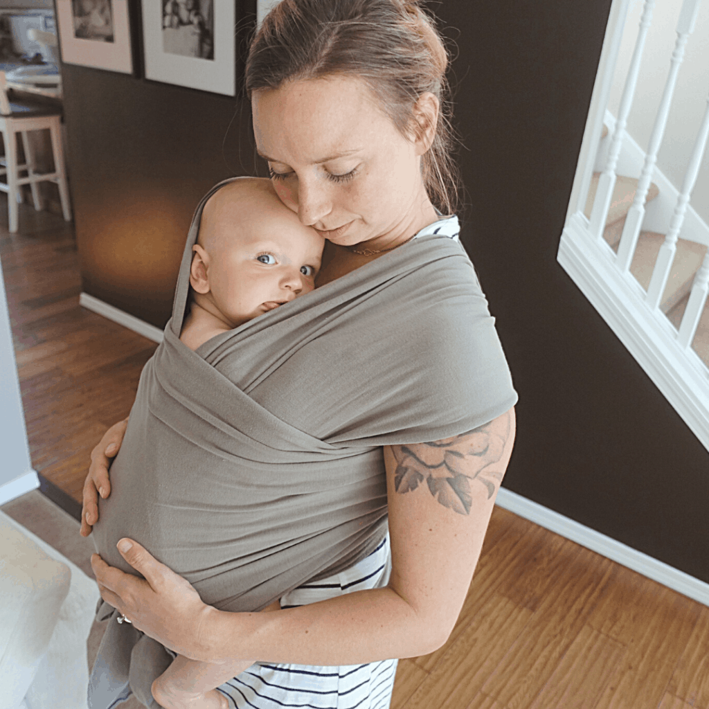 mother and son in grey boba baby wrap son smiling at camera mom resting head on his head