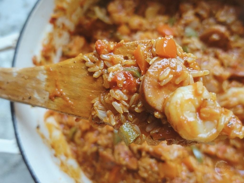 a scoop of jambalaya on a wooden spoon with a dutch oven in the background