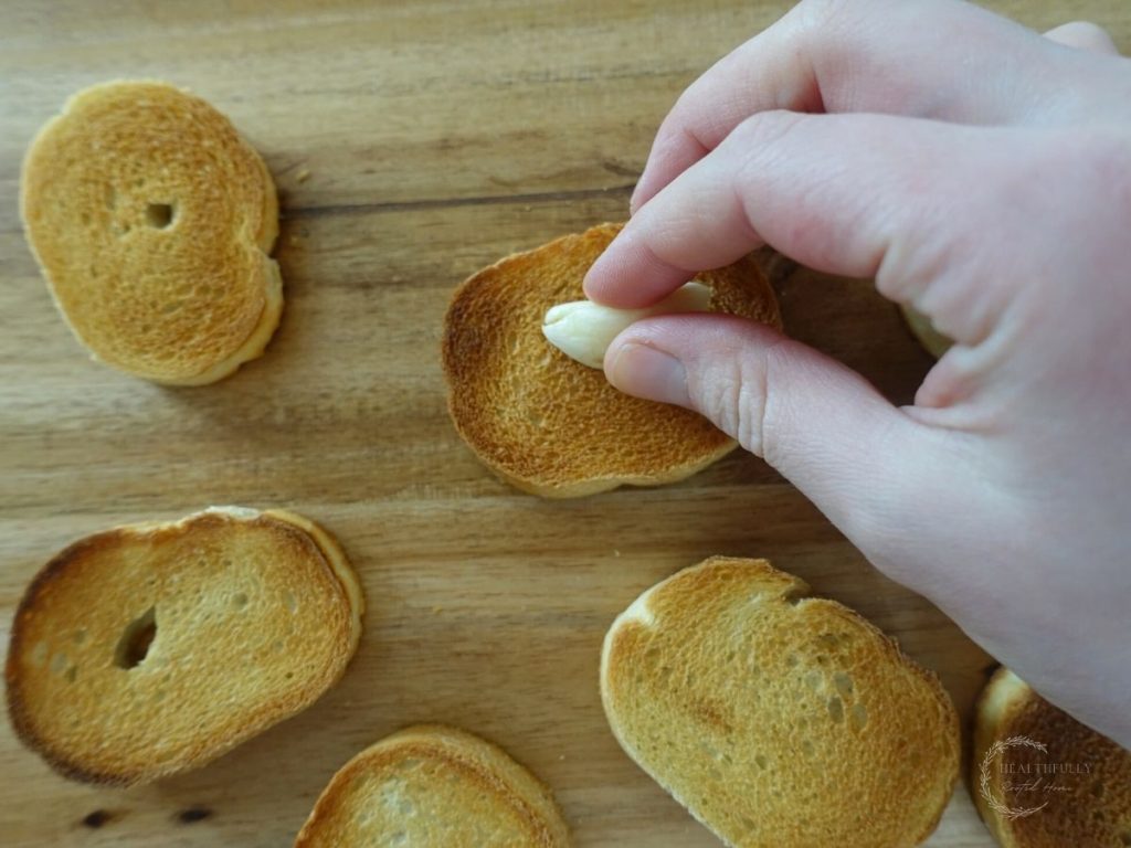 rubbing toasted crostini with garlic cloves on a wooden cutting board