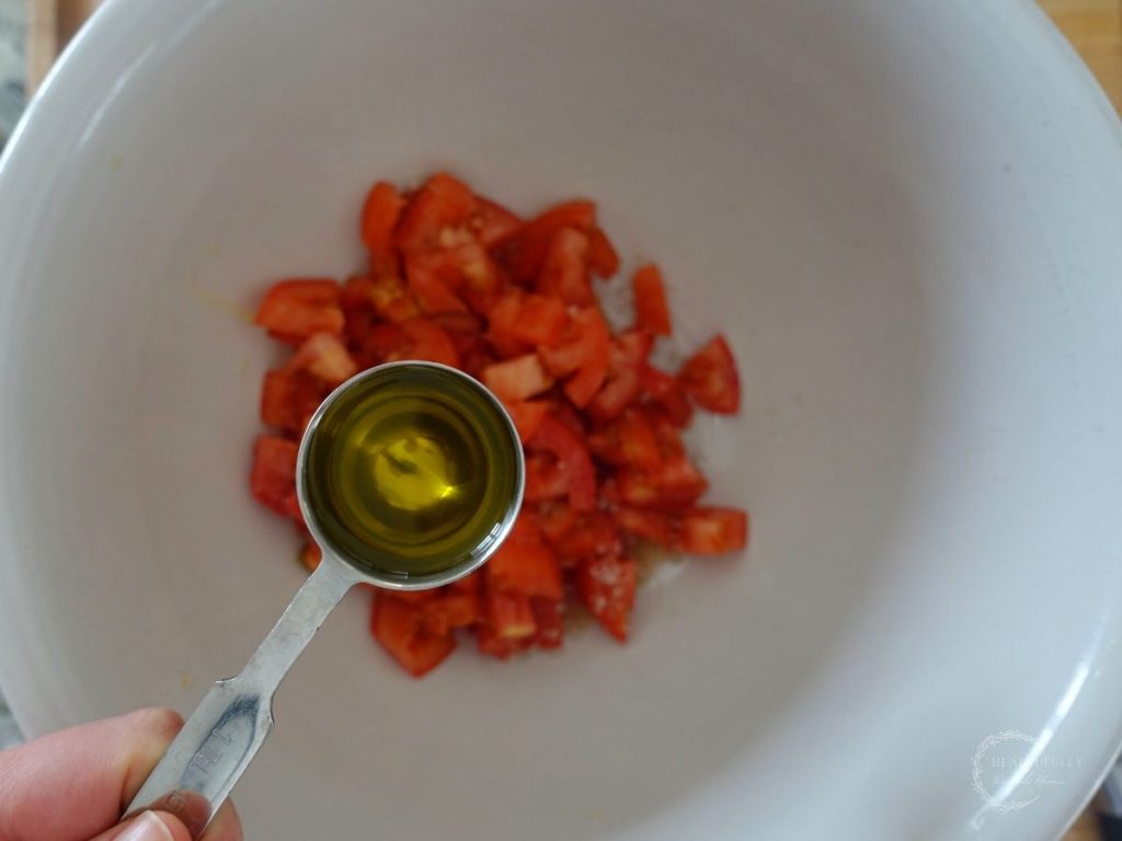 diced tomatoes in a bowl adding olive oil from a measuring spoon