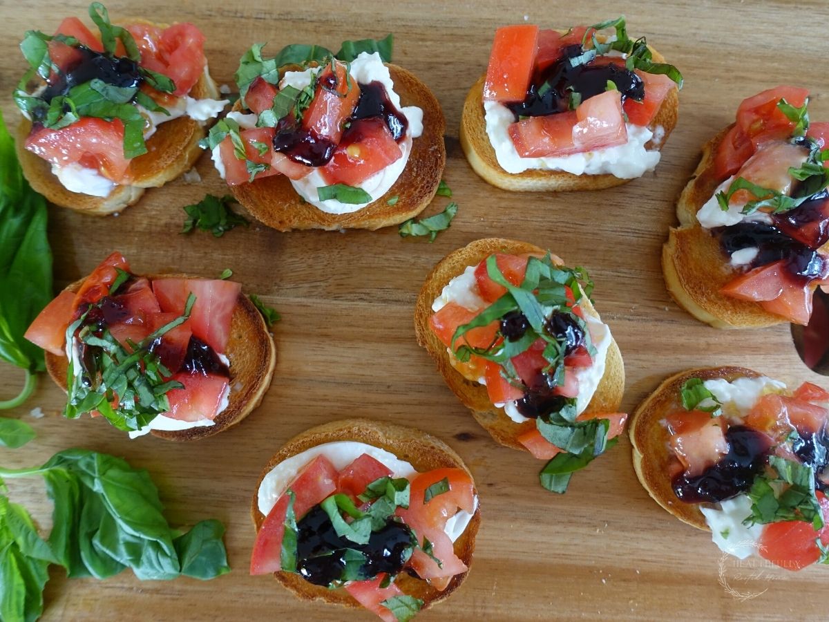 burrata bruschetta italiana on a wooden cutting board with basil leaves on the side and drizzled with balsamic fig glaze
