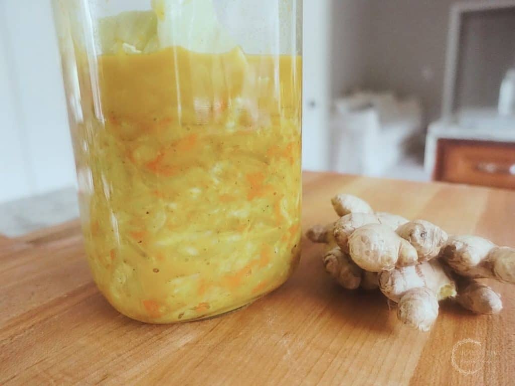 curry kraut in a glass fermenting jar on top of a boos block cutting board next to a ginger root