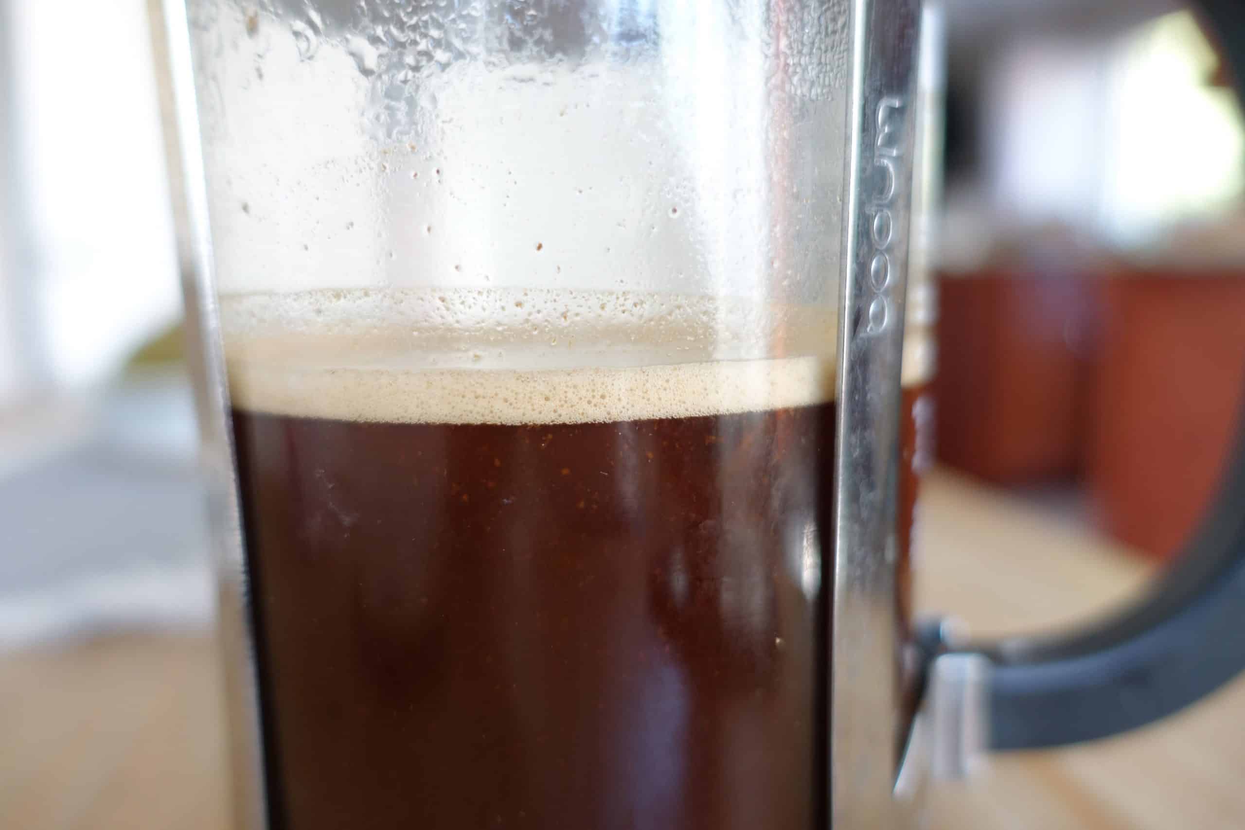 french press coffee plunger pushed down and coffee fully steeped with a layer of crema on top