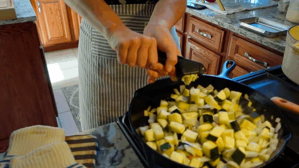 using garlic press for minced garlic into cast iron skillet wearing striped apron