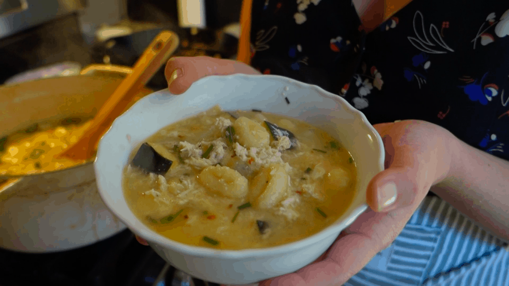 holding a bowl of lemon chicken gnocchi soup with zucchini and chives