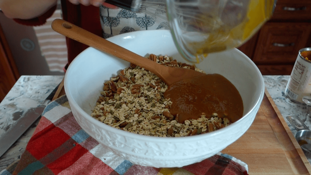 combining the wet and dry ingredients for pumpkin spice granola bark in a large white bowl on top of a butcher block with a red checkered tea towel